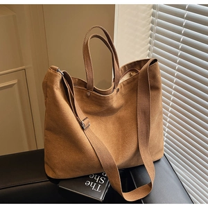Close-up of brown canvas tote bag featuring metal rivets and adjustable shoulder strap