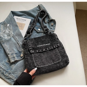 Dettaglio borsa a tracolla in denim nero lavato con scritta bianca e fibbia in metallo fissa