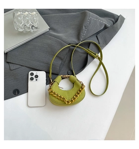 Mini bolso media luna verde con cadena dorada junto a un iPhone para comparar el tamaño