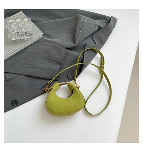 Detalle del mini bolso de media luna verde oliva con cierre dorado sobre traje gris