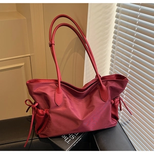 Détail d'un sac de voyage rose foncé en nylon avec poignées en cuir sur un canapé noir