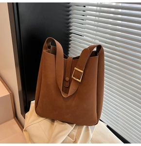 Detail of caramel brown leather bucket bag featuring a gold square buckle and wide strap