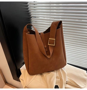 Macro detail of brown suede tote bag featuring adjustable wide strap with golden buckle