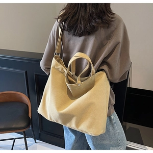 Large khaki canvas tote bag with shoulder strap and handles shown on a model