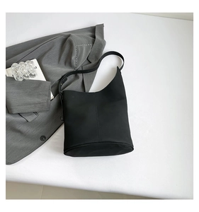Minimalist black bucket bag with adjustable strap and vertical stitching on white background