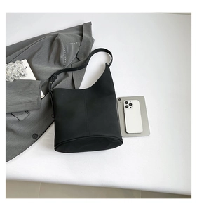 Minimalist black bucket bag with adjustable strap shown next to a smartphone for size reference