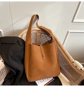 Close-up of brown faux suede tote bag with wide shoulder strap on a rattan chair