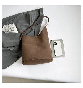 Flat lay of brown suede bucket bag with adjustable strap and minimalist urban accessories