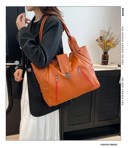 Close-up of orange faux leather tote bag with decorative zippers and flower metal charm