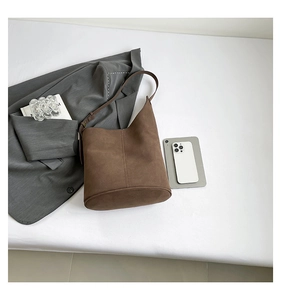 Detailed view of brown suede bucket bag with vertical stitching on minimalist white surface
