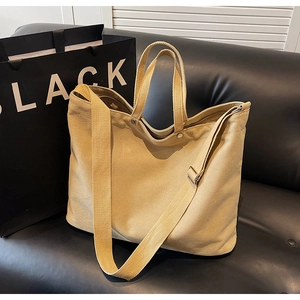 Khaki canvas tote bag with adjustable shoulder strap resting on a black leather sofa