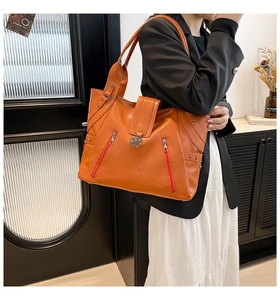 Detail of orange lychee grain tote bag with diagonal zippers and metal flower logo charm