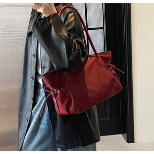 Grand sac de voyage rouge avec cordon de serrage porté par un mannequin en manteau de cuir noir