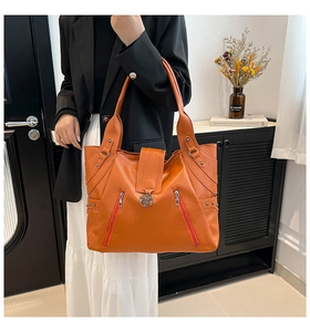 Detail of orange PU leather tote bag featuring decorative zippers and metal rivets