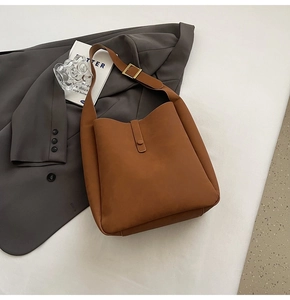 Detailed close-up of brown suede shoulder bag with gold metallic buckle and wide strap