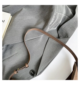 Close-up of brown textured leather bag strap and grey tailored suit fabric with white stitching