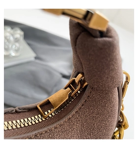 Detalle de bolso medialuna en ante marrón con cadena dorada y cremallera de bronce