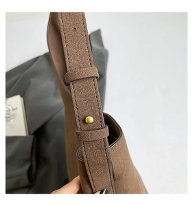 Detailed close-up of brown suede shoulder strap with a minimalist gold metal stud buckle