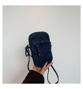 Detail of a dark blue denim crossbody phone bag with drawstring pocket and zipper