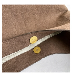 Macro view of golden cylindrical magnetic closure and brown suede texture on shoulder bag
