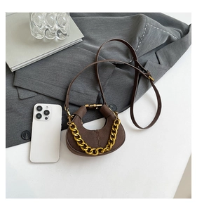 Detalle de mini bolso de media luna marrón oscuro con cadena dorada y fondo minimalista