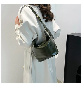 Close-up of deep green glossy leather shoulder bag with adjustable strap and gold buckle
