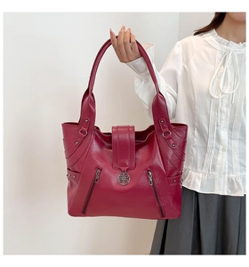 Detail of burgundy tote bag showing textured leather, metal rivets and floral hardware emblem