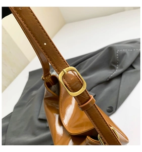 Detail of adjustable brown leather shoulder strap with golden metal buckle and stitching