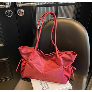 Détail du sac de voyage rouge avec cordons latéraux sur une chaise noire texturée