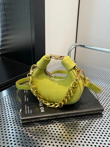 Bolso mini media luna verde chic con correa de cadena dorada sobre libro negro