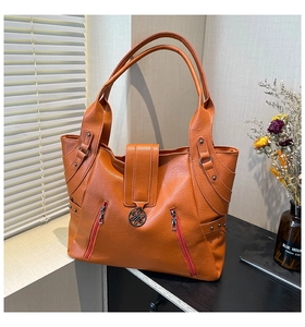 Detail view of orange PU tote bag with metal floral twist lock and zipper pockets