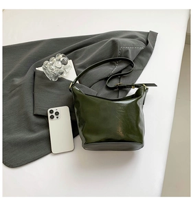 Detail of dark green glossy leather bag with metal buckle on grey fabric background