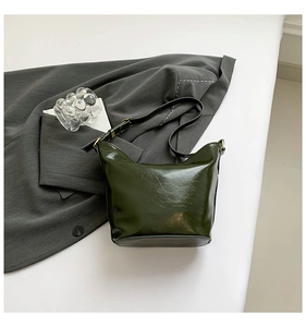 Detail of dark green bucket bag showing glossy wrinkled leather texture and gold hardware