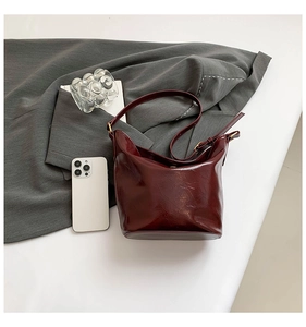 Detail view of deep red patent leather shoulder bag with vintage crinkle texture and gold buckle