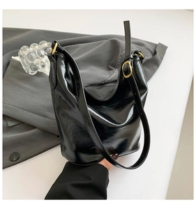 Detail of black glossy wrinkled hobo bag with gold buckle on grey fabric background