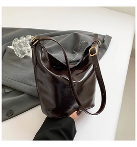 Detailed view of dark brown patent leather bucket bag with shiny texture and gold hardware
