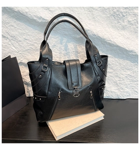 Detail view of black lychee grain leather tote bag with metal flower clasp and side zippers