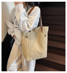 Detalle del bolso tote de lona caqui con asas de cuero marrón y bolsillo con remaches
