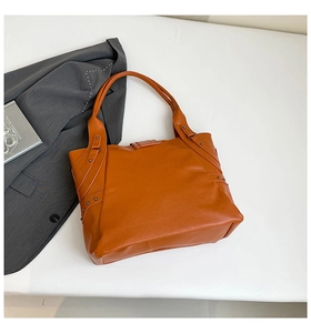 Close-up of orange textured PU tote bag with metal rivet details and reinforced stitching