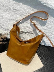 Vintage brown patent leather hobo bag with adjustable strap on a textured rock surface