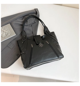 Detailed close-up of black leather tote bag with metallic flower buckle and side zippers