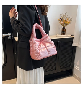 Side view of a pink quilted down shoulder bag being worn by a model in a modern interior