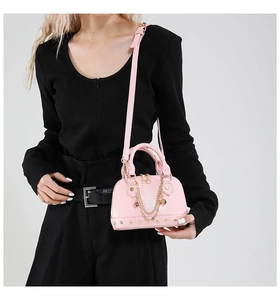 Detailansicht einer rosa Muscheltasche mit Goldkette und Nieten, präsentiert am Modell