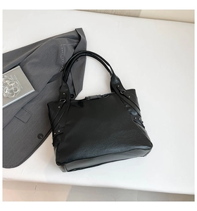 Flat lay of black pebbled leather tote bag with rivet straps on a clean white background