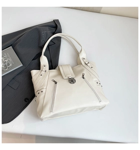Detail of cream tote bag with pebble texture, decorative zippers, and rivet accents