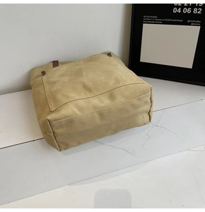 Close-up of khaki canvas tote bag with brown leather handles and spacious front pocket