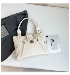 Detail view of large cream PU tote bag with floral pendant and zip accents on a flat lay