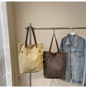 Detail of beige and dark brown canvas tote bags with leather straps and front pockets