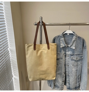 Beige canvas tote bag with brown leather straps hanging on a metal rack outdoors