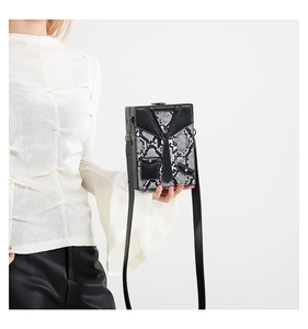 Detail view of snakeskin pattern box bag with creative 3D tie design and black strap